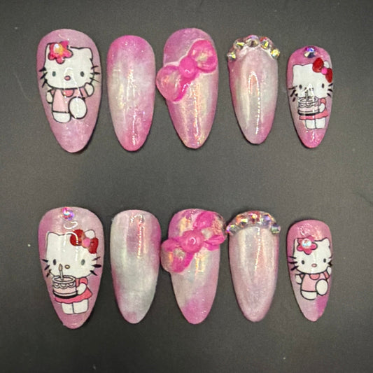 A set of 10 press-on nails featuring Hello Kitty designs, arranged in two rows of five on a dark gray background. The nails are primarily pink with white glitter, featuring Hello Kitty character illustrations and 3D pink bows.